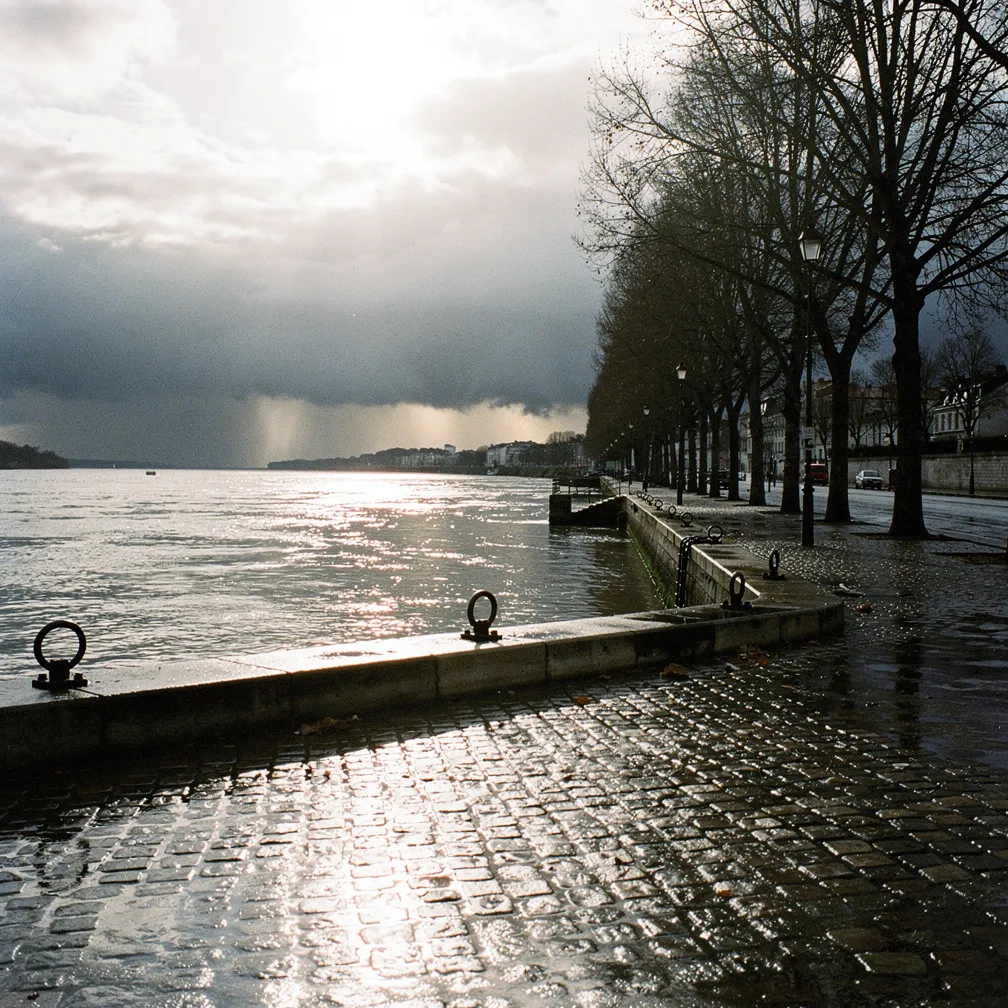 Les quais de Loire à Nantes sous un ciel changeant, une averse au loin sur l’estuaire